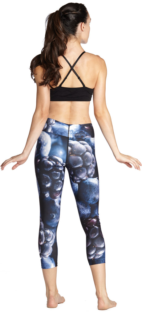 Model wearing leggings printed with a macro image of bluberries and blackberries. The colors are rich deep blues and purples.