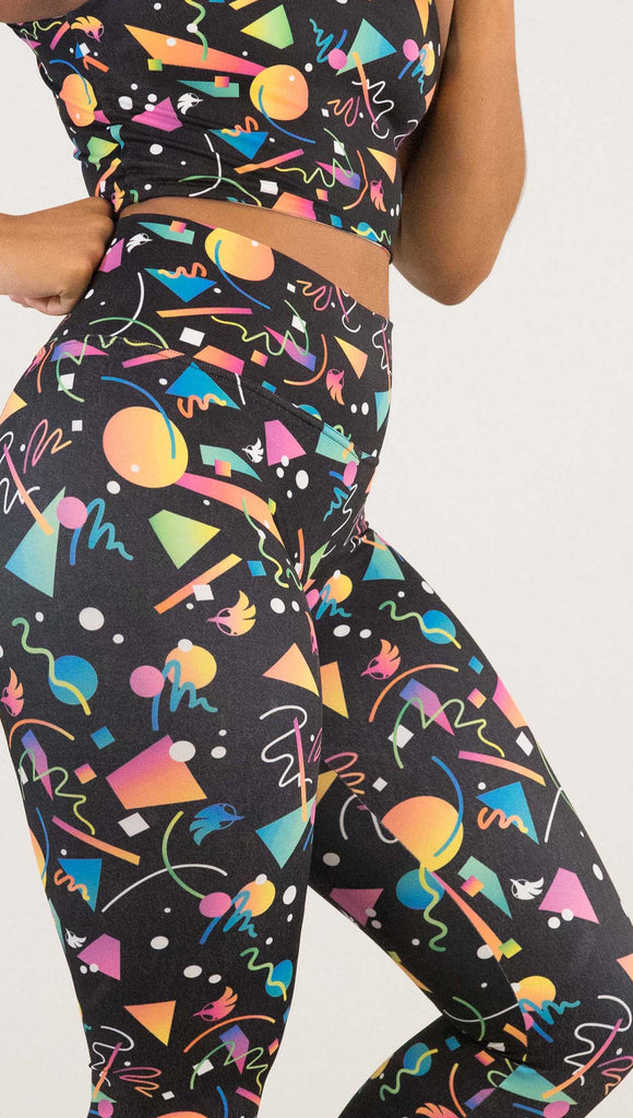 Zoomed in photo of model wearing WERKSHOP white confetti athleisure leggings. The artwork on the leggings shows multi-colored circles, scribbles and triangles over a black background.