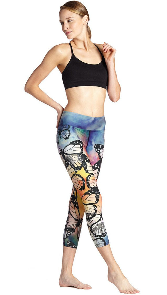 slightly turned front view of model wearing colorful butterfly themed printed capri triathlon leggings and sports top