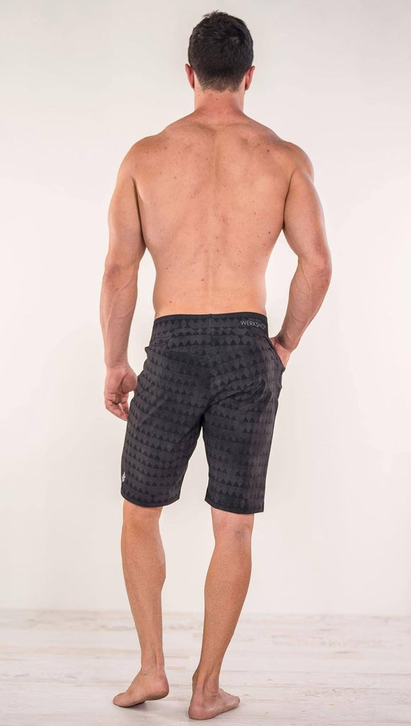 Back view of model wearing charcoal black printed performance shorts with slim fit and distressed tribal inspired art