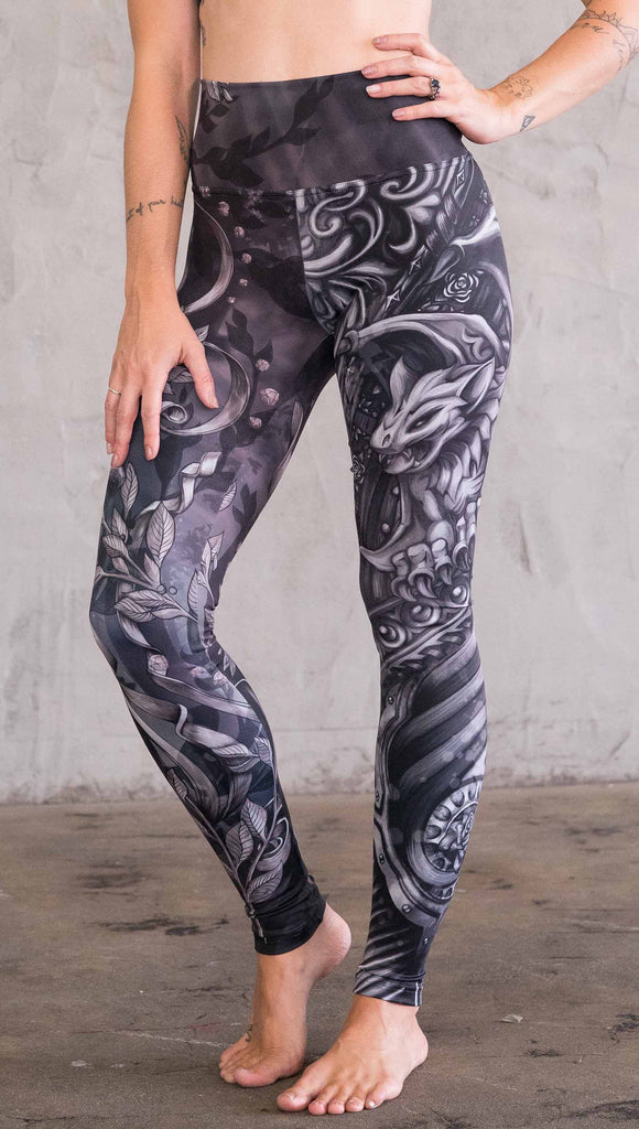 Model wearing the gargoyle/ gothica mashup athleisure leggings in a black and gray color. One leg has skulls and the other leg has a gargoyle