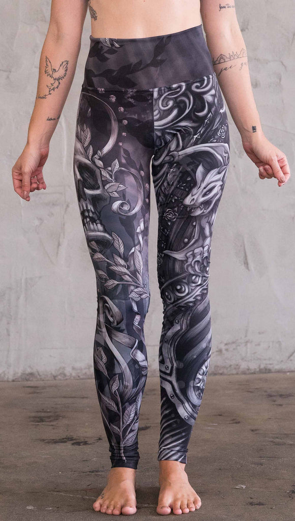 Front view of model wearing the gargoyle mashup leggings in a black and gray color. One leg has a gargoyle and the other leg has a large skull 