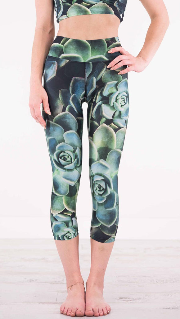 Front view of model wearing black capri leggings with green succulent plants throughout