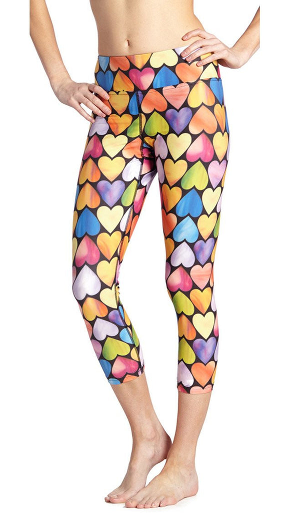 close up front view of model wearing colorful heart themed printed capri leggings