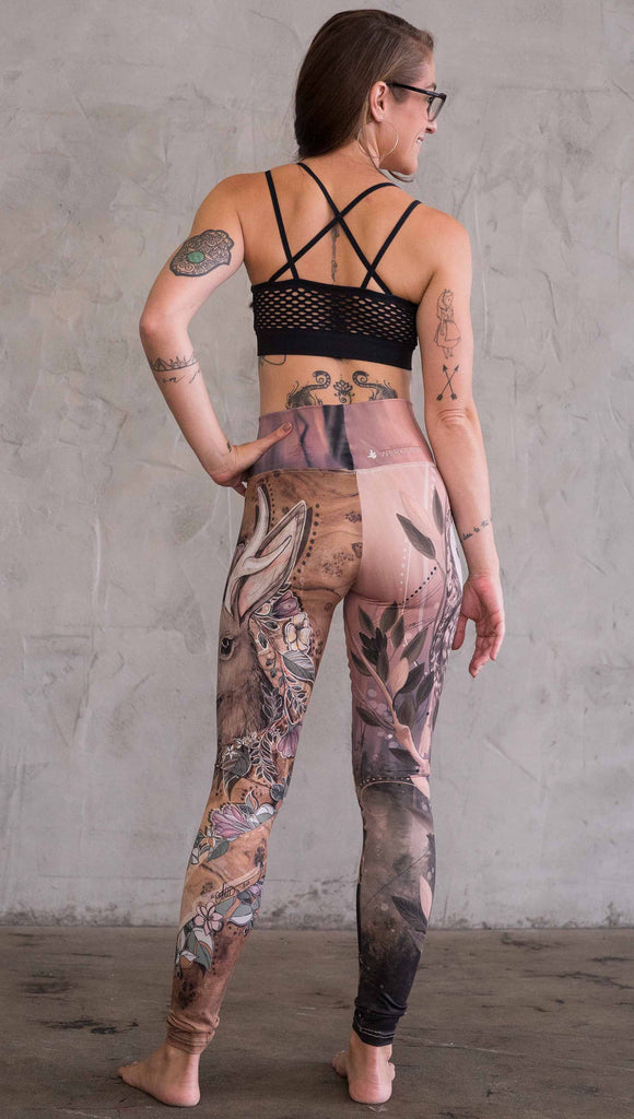 Zoomed out back view of model wearing the jackalope mashup leggings in a light mauve and brown color. One leg has a owl and the other leg has a jackalope
