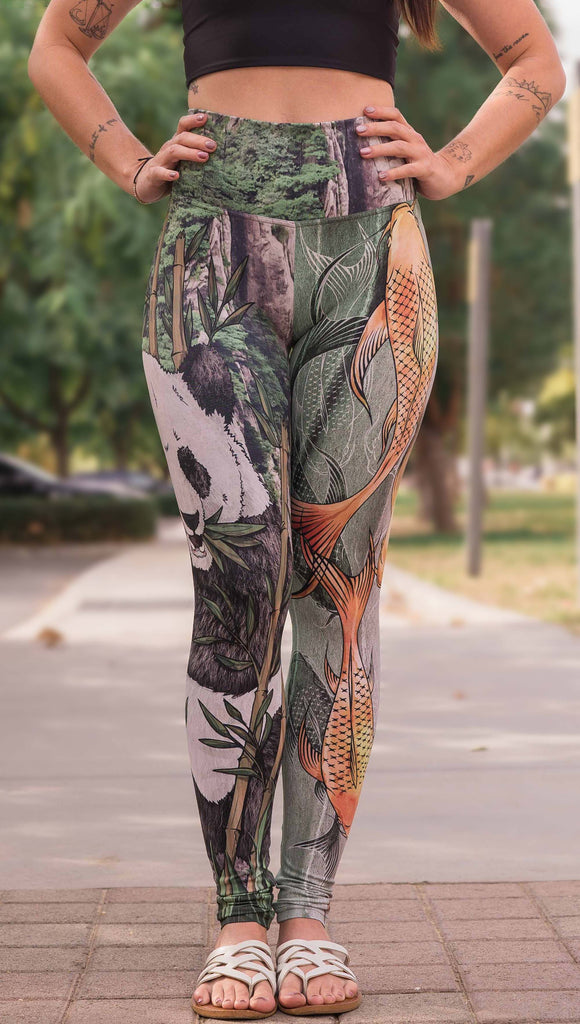 Model wearing WERKSHOP Koi Fish and Giant Panda Mashup Leggings. The wearer's right leg has an illustration of a panda eating bamboo with a gorgeous background of mountains. The wearers right leg has koi fishies swimming over an abstract taupe and forest green background.