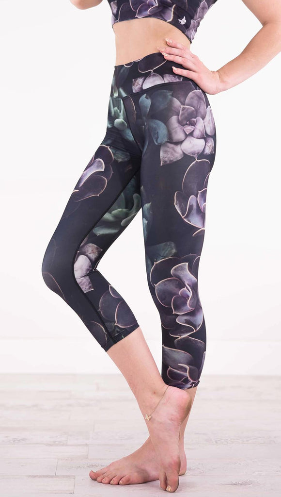Left view of model wearing black capri leggings with green and purple succulent plants throughout
