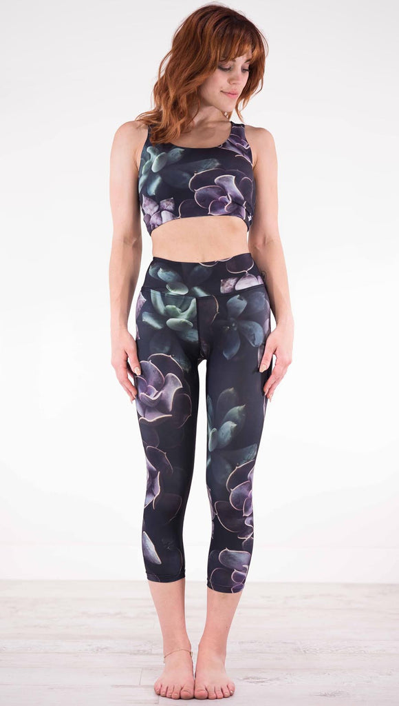Front view of model wearing black capri leggings with green and purple succulent plants throughout
