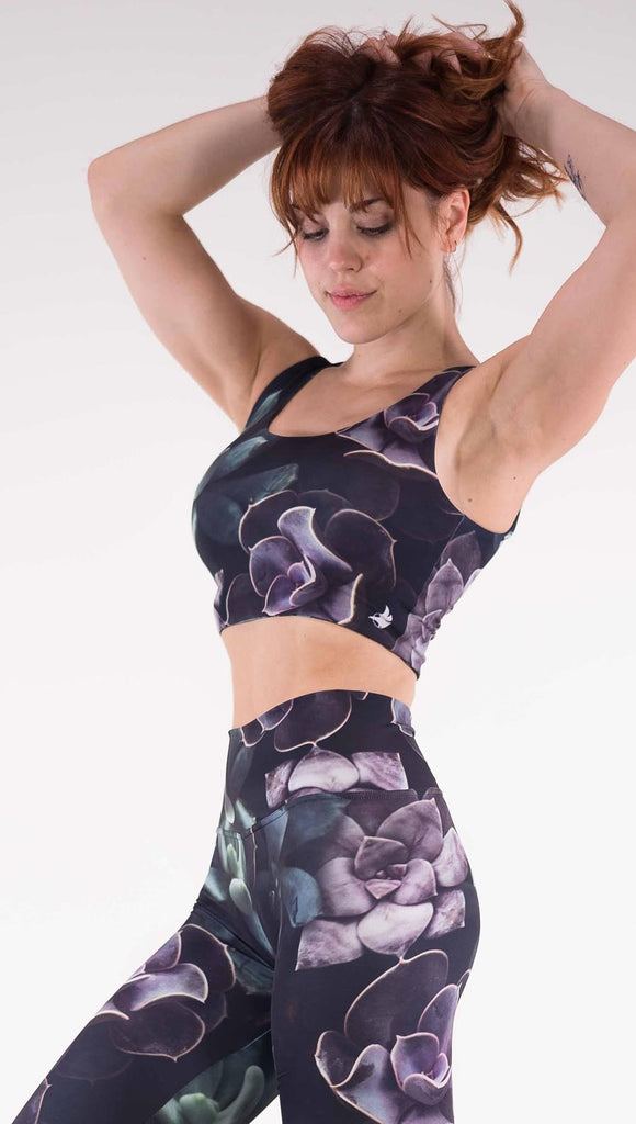Left view of model wearing the Midnight Garden reversible top. This is in the Midnight Garden side, it is a black crop top with green and purple succulent plants throughout