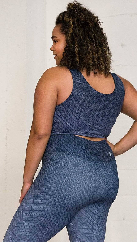 Three quarter length left rear view of a model wearing a blue mosaic tile print reversible crop top with dark gray mosaic tile print on the other side 