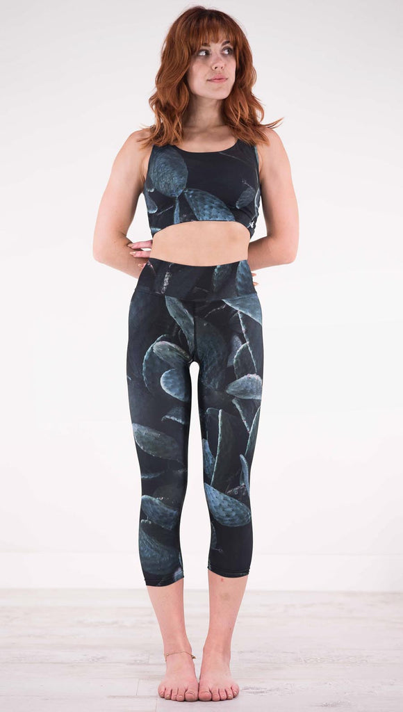 Front view of model wearing black capri leggings with dark green cacti plants throughout