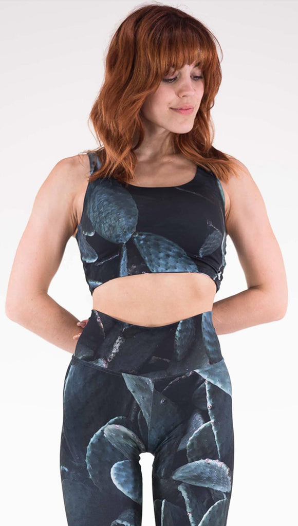 Front view of model wearing the Midnight Garden reversible top. This is in the Prickly Pair side, it is a black crop top with dark green cacti plants throughout