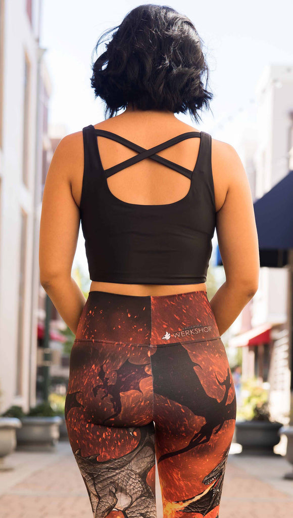 Model wearing WERKSHOP Spitfire Leggings. The artwork on the leggings features a detailed fire breathing dragon blowing flames into a forest with a bright red sky filled with floating embers and silhouettes of more dragons flying in the background. She is wearing our black/royal blue featherlight top.