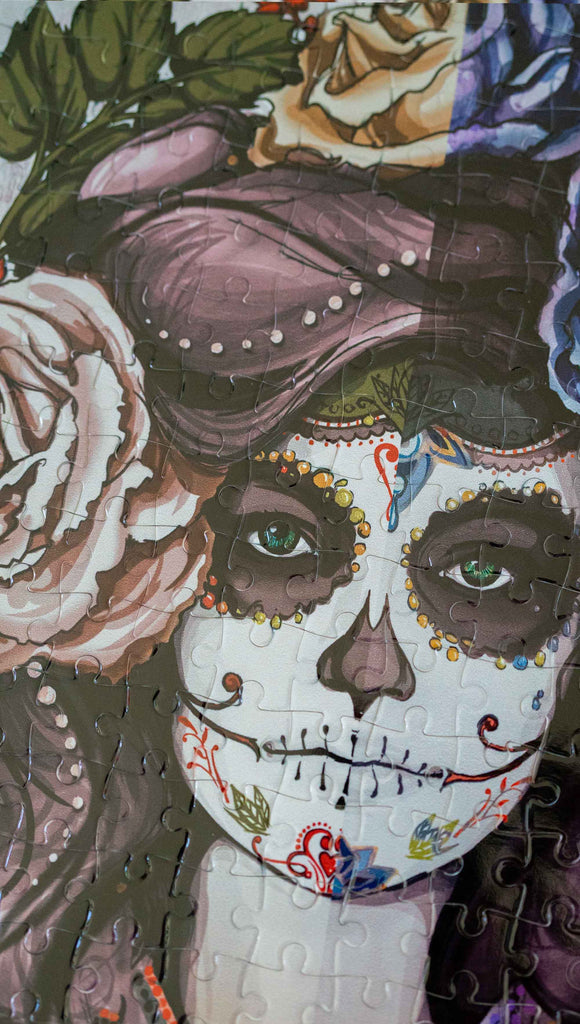 Zoomed in photo of WERKSHOP Sugar Skull Mashup Puzzle. The artwork celebrates Dia De Los Muertos with a drawing of a girl wearing sugarskull makeup surrounded by a wreath of roses.