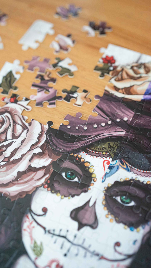 Partially disassembled WERKSHOP Sugar Skull Mashup Puzzle. The artwork celebrates Dia De Los Muertos with a drawing of a girl wearing sugarskull makeup surrounded by a wreath of roses.