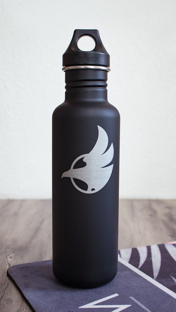 Black water bottle with Eagle Rock Werkshop logo resting on a purple yoga mat with Eagle Rock Werkshop logo.