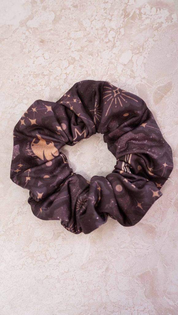 Zodiac theme printed hair scrunchie with zodiac themed artwork with the sun and moon with the moon phases, shooting stars and all 12 zodiac constellations in gold over a dark purple background.