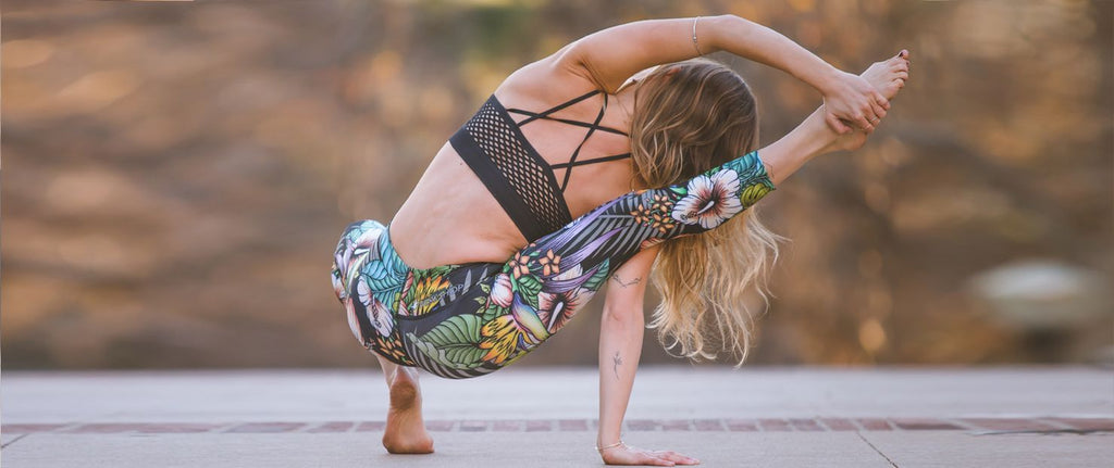 Woman doing an advanced yoga compass pose while wearing WERKSHOP Floral Night Triathlon Capri Leggings