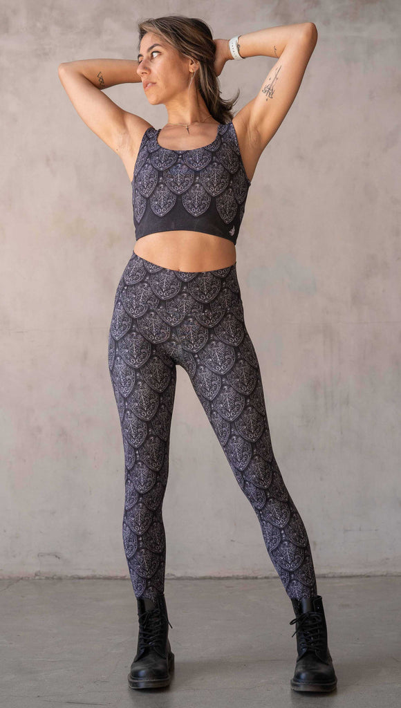 Full body front view of model wearing WERKSHOP Dragon Rider leggings in Silver. The artwork features an intricate battle shield designed to look like dragon scales. This color way is all shades of black and gray.