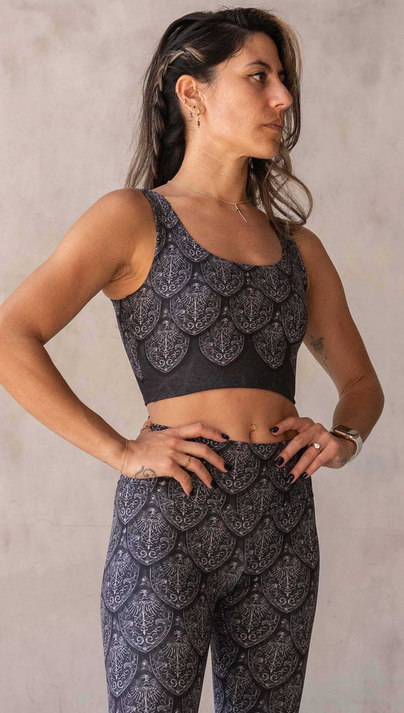 Front view of model wearing WERKSHOP Dragon Rider reversible Top. One side of the top is gray/silver tone and the opposite side is gold/bronze. The artwork features an intricate battle shield designed to look like dragon scales. This photo shows the silver side of the top.