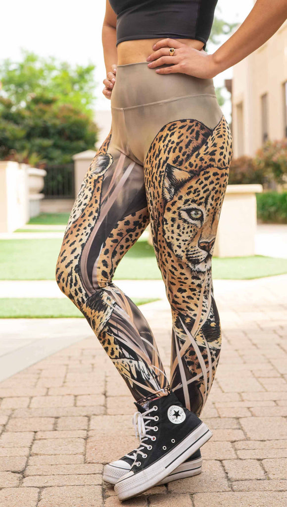 Model wearing WERKSHOP Leopard Legings. The leggings feature original and exclusive artwork of a Leopard walking through the brush. The leggings are all khaki and tan tones with little pops of green in the leopards eyes.