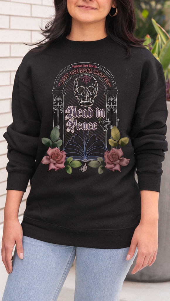 Person wearing a black sweatshirt with a 'Read in Peace' design featuring a skull and flowers over a tombstone with the phrase, "Famous Last Words: Just One More Chapter" 