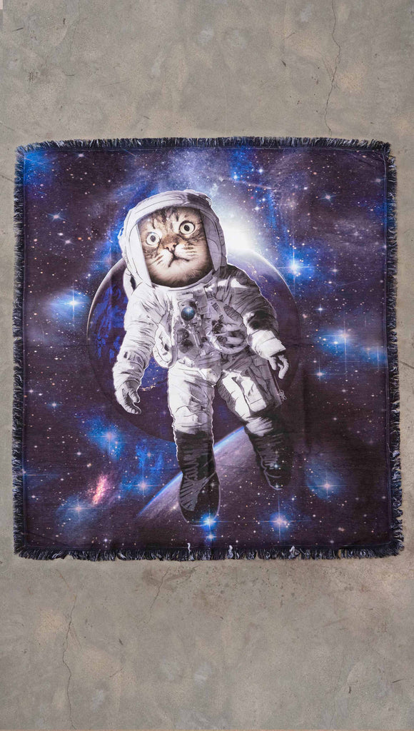 Decorative Chenille Tapestry printed with limited edition artwork by our Female Founder, Chriztina Marie. The artwork features an adorable domestic house cat wearing an astronaut uniform, floating in outer space with a nebula behind him. This photo shows it laid flat on the floor.