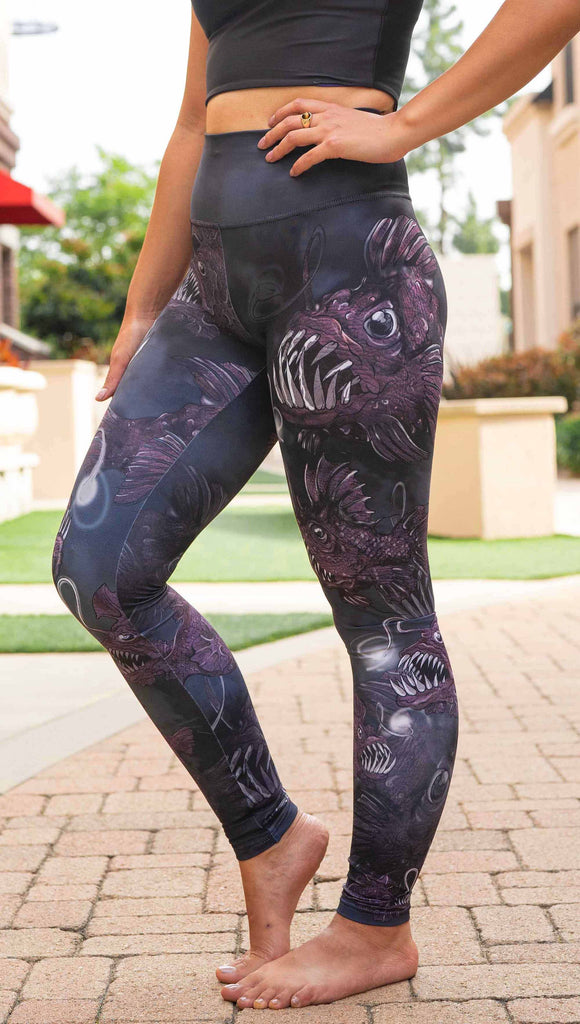 Girl wearing WERKSHOP Angler Fish Athleisure Leggings. The artwork on the leggings feature pink hued/textured angler fish over a black and gray airbrushed background