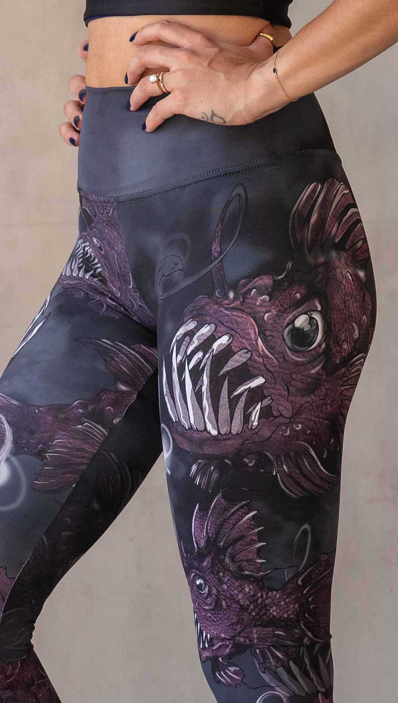 zoomed in image of girl wearing WERKSHOP Angler Fish Athleisure Leggings. The artwork on the leggings feature pink hued/textured angler fish over a black and gray airbrushed background