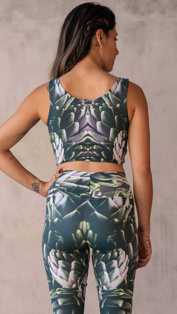 irl wearing the WERKSHOP Reversible Artichoke and Rosaline Top. This image shows the Artichoke side. It has pops of bright green and bright purple over a mostly dark green base. It is a very geometric and fractal design.