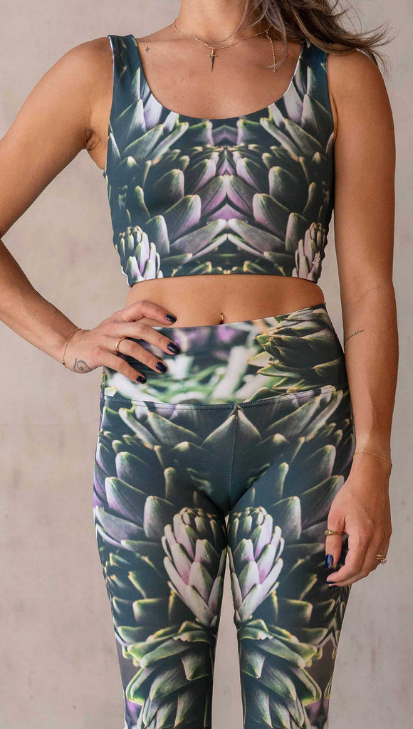zoomed in image of girl wearing WERKSHOP Artichoke Athleisure Leggings. The leggings show a photo-real fractal inspired edit of artichokes. It has pops of bright green and bright purple over a mostly dark green base. It is a very geometric and fractal design.