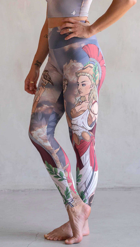 Side view of model wearing WERKSHOP Athena leggings. The leggings are printed with original artwork by Chriztina Marie and features Athena, the goddess of war standing on a cliff’s edge. She is holding a spear with one hand and her owl with the other. She is wearing a greek goddess dress/warrior hat with colors of cream, gold and red. Behind her is a beautiful cloudy sky with rays of light shining down onto her. The model is also wearing a matching top.
