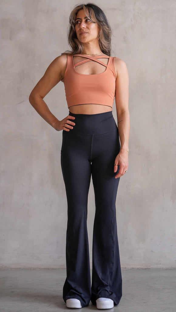 Model wearing WERKSHOP Black EnviSoft Bells. The pants feaure a belled leg opening, flatlock seams, pockets on each thigh, a long panel gusset and small silver eagle logo on the right pocket.