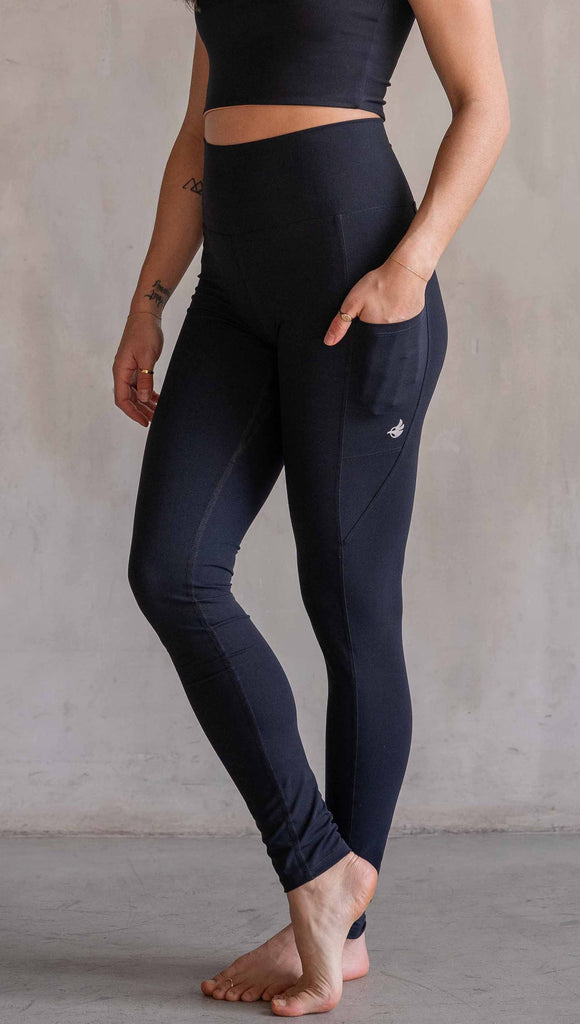 Model wearing WERKSHOP Solid Black EnviSoft Leggings. Featuring pockets on each thigh, a long panel gusset, flatlock seams and an eagle logo on the right pocket.