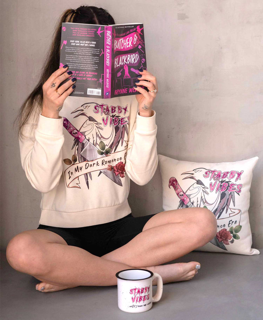 Girl sitting on the floor while reading a book. She is wearing a WERKSHOP Stabby Vibes Hoodie and Black Bicycle Length Shorts.