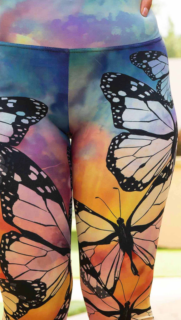 Zoomed in photo of girl wearing WERKSHOP Butterflies Athleisure Leggings. The artwork on the leggings features a black outline of monarch butterflies over a rainbow coloured watercolor background.