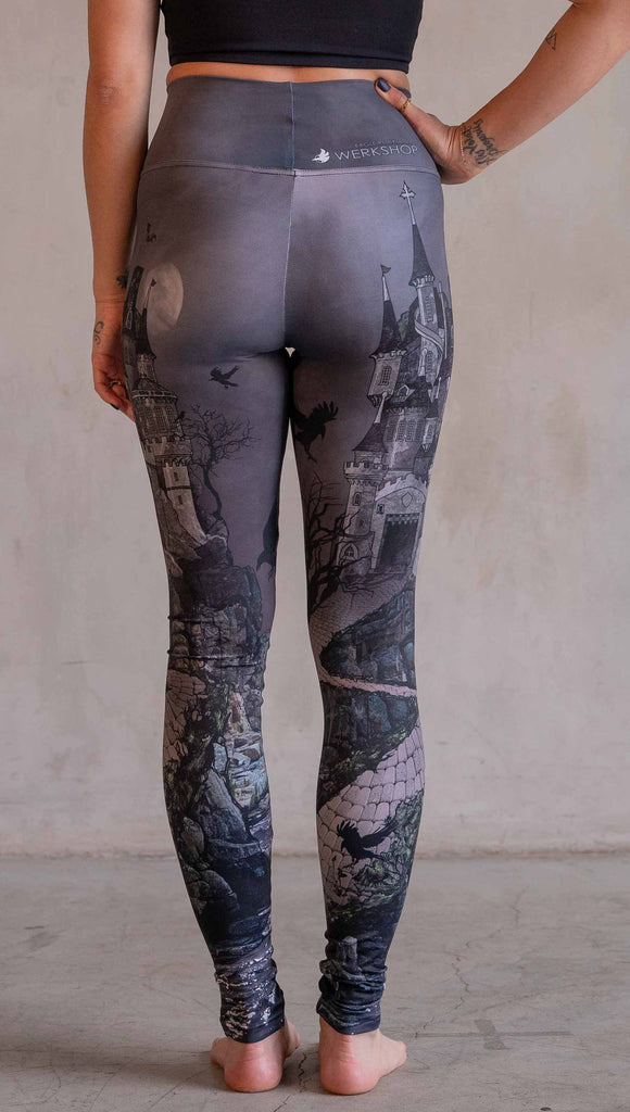 Model wearing WERKSHOP Dark Castle Leggings. The artwork on the leggings feature a fully monochrome (black and gray) gothic castle with stone walkway and crows flying in the moonlight.