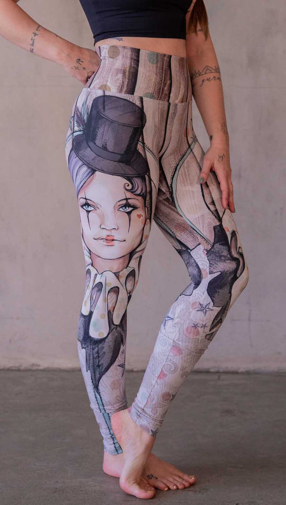 Model wearing WERKSHOP Circus Girl Leggings. Featuring artwork of a circus girl wearing a top hat, ruffled collar with mime makeup over a polka dot and woodgrain background.