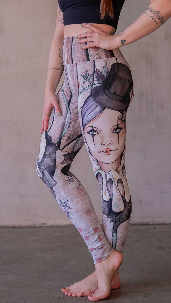 Model wearing WERKSHOP Circus Girl Leggings. Featuring artwork of a circus girl wearing a top hat, ruffled collar with mime makeup over a polka dot and woodgrain background.