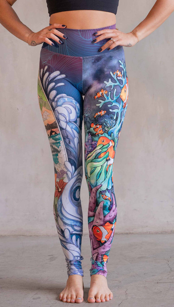 Model wearing WERKSHOP Clownfish and Surf Mashup Leggings. These leggings feature two iconic prints. on the right leg, you have a surfboard with dolphins and spashing waves. On the left leg, you have an explosion of color with a coral reef and clownfish.