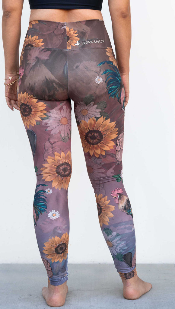 Model wearing WERKSHOP "Cocks n Beavers" Leggings. The leggings show hand painted artwork of roosters and beavers with daisies and sunflowers over an ombreback ground that goes from a warm brown on top to slate blue at the leg opening.