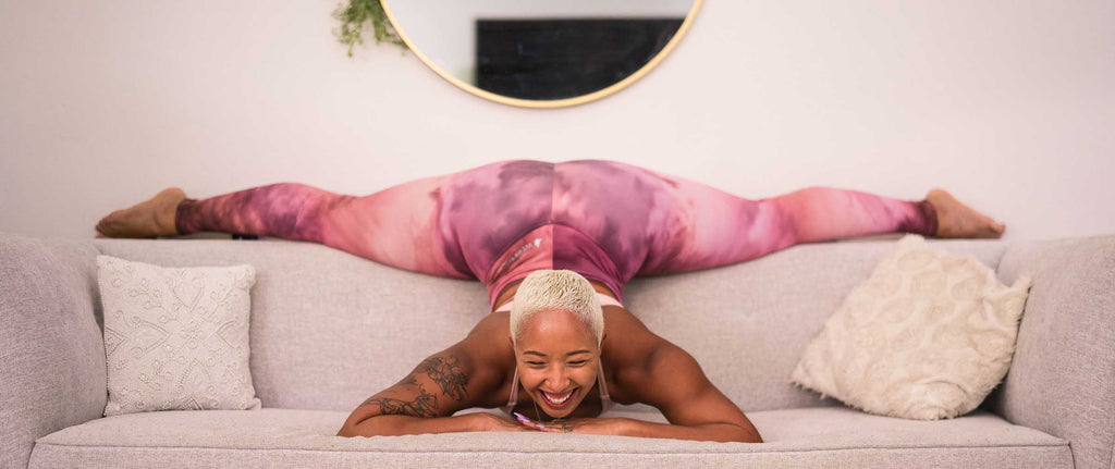 Girl laughing on a couch while doing the splits and wearing WERKSHOP rose quart athleisure leggings and vanilla sports bra