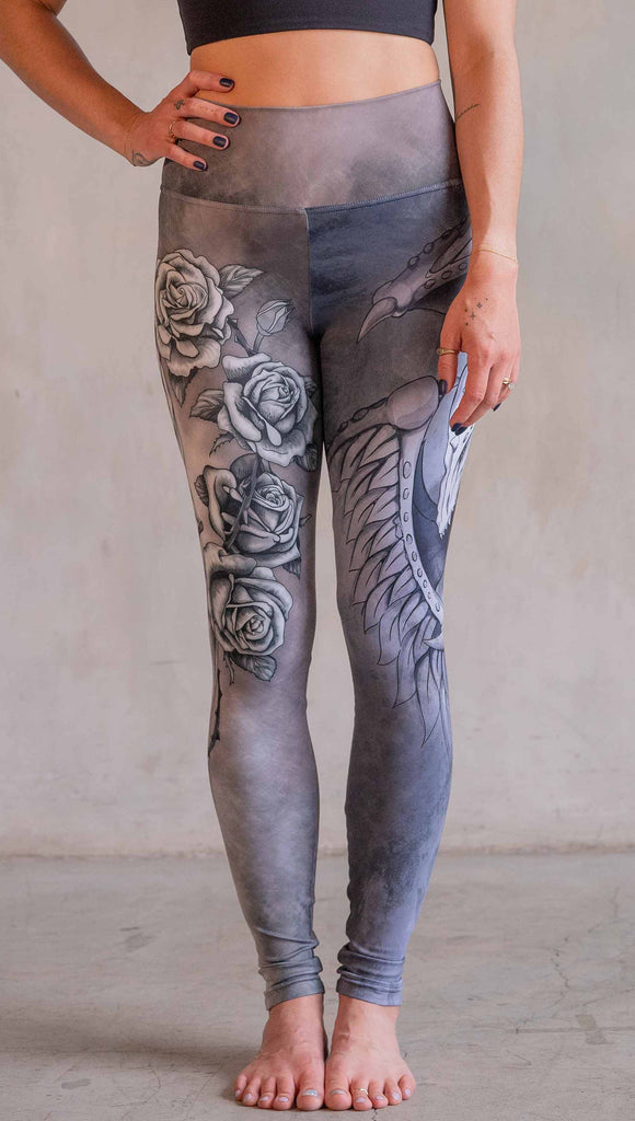 Model wearing WERKSHOP Dagger Mashup Leggings. One leg has a dagger with a wreath of roses. The other leg has an abstract gargoyle-esc dragon. Both legs are neutral in color tone with the right leg being a bit taupe and the left leg being a cool gray.