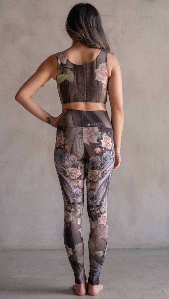 Model wearing WERKSHOP Dark Unicorn Athleisure Leggings. The leggings feature original artwork of a unicorn surrounded by a wreath of vintage coloured roses. The unicorn has a beaded chain with a skull dangling from it's horn. The artwork is over a warm woodgrain background.