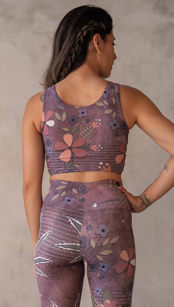 Model wearing WERKSHOP Dope + Flowers Reversible top. One side of the top features patchwork daisys over grainy mauve toned leather background. The opposite side of the top features marijuana leaves over a warm brown background. Both legs have faux stitching and a small eagle logo on the bottom left sweep.