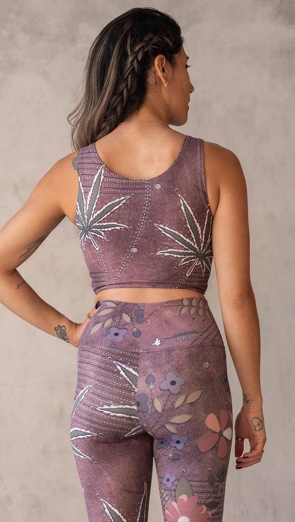Model wearing WERKSHOP Dope + Flowers Reversible top. One side of the top features patchwork daisys over grainy mauve toned leather background. The opposite side of the top features marijuana leaves over a warm brown background. Both legs have faux stitching and a small eagle logo on the bottom left sweep.
