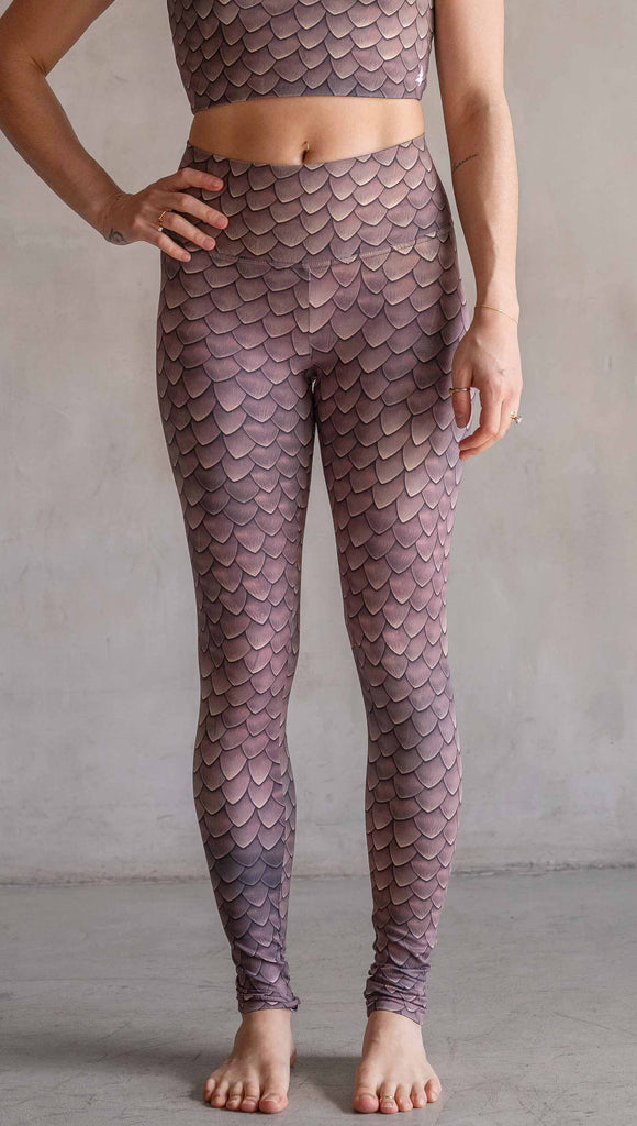 Model wearing WERKSHOP Dragon Scales leggings. The artwork on the leggings features small pointed scales in a warm taupe/gold color pallet.