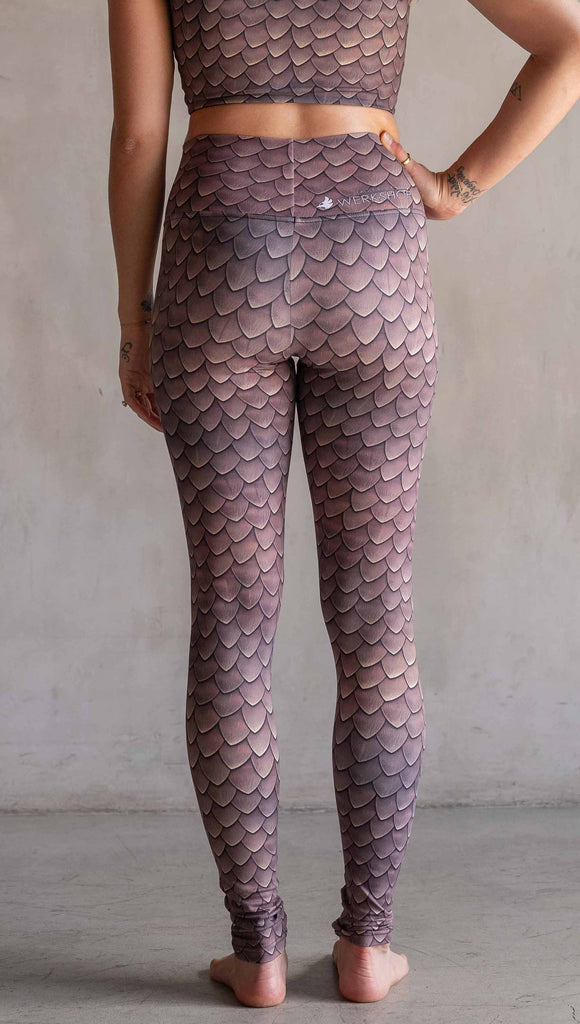 Model wearing WERKSHOP Dragon Scales leggings. The artwork on the leggings features small pointed scales in a warm taupe/gold color pallet.