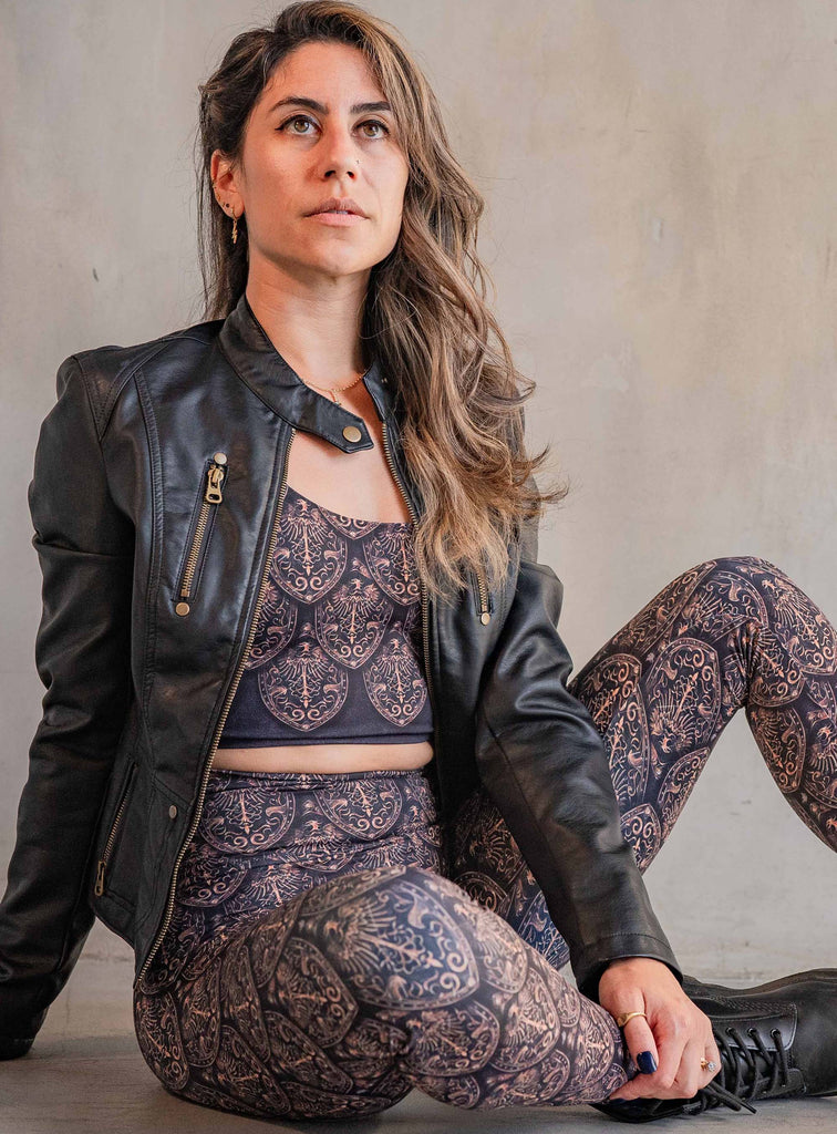 Model casually sitting on the floor while wearing WERKSHOP Dragon Rider set in Gold. The artwork features an intricate battle shield designed to look like dragon scales. This color way is all shades of gold and bronze.