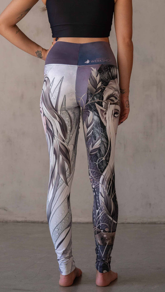 Model wearing WERKSHOP Elf + Sorceress Mashup leggings. The leggings are printed with original artwork by Chriztina Marie. One leg features a dark forest elf wearing a fur trimmed cloak. The other leg features a winter sorceress holding an orb with frosted purples and lavender tones.